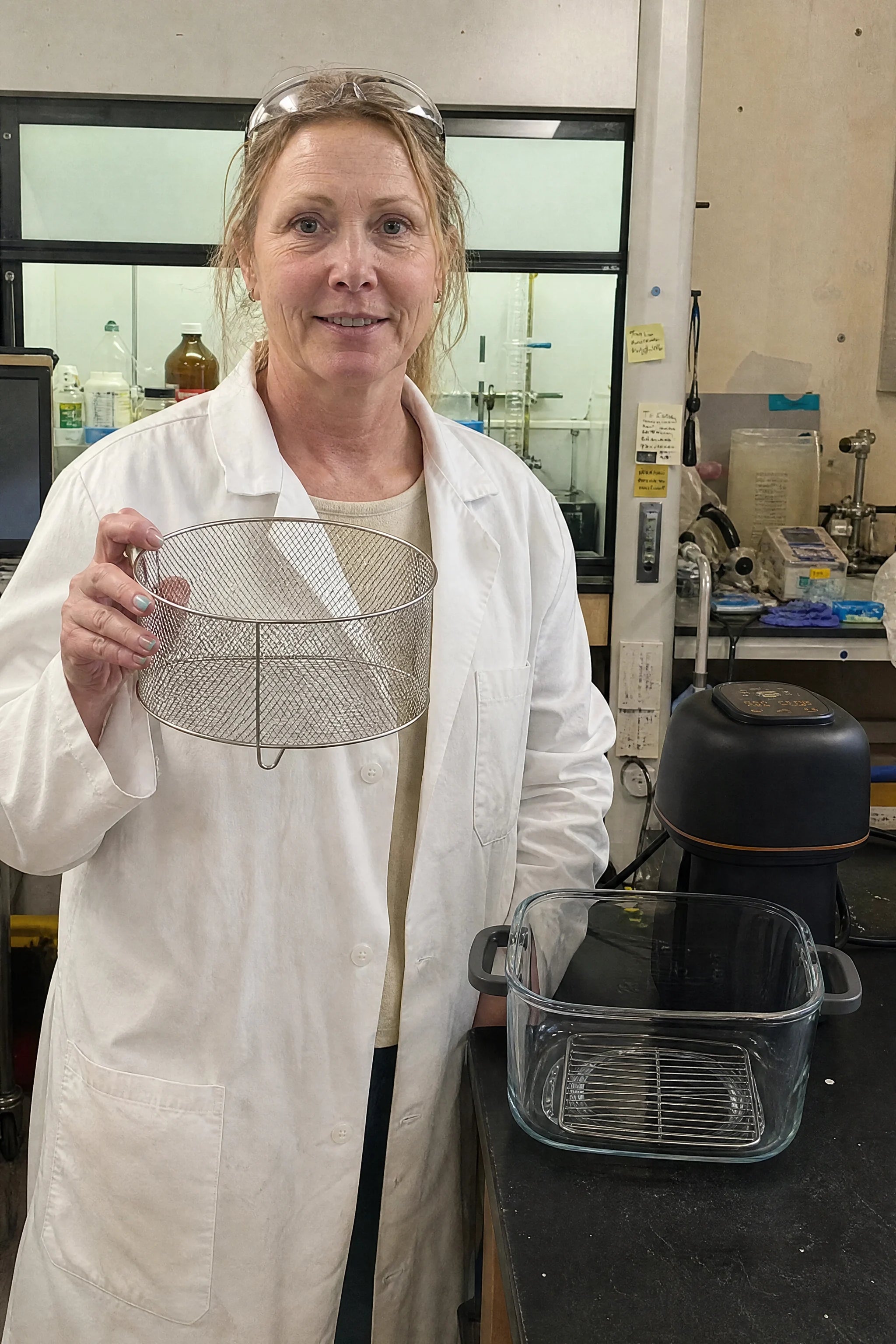 A materials chemist in her lab holding the stainless basket of Kaldera Glass