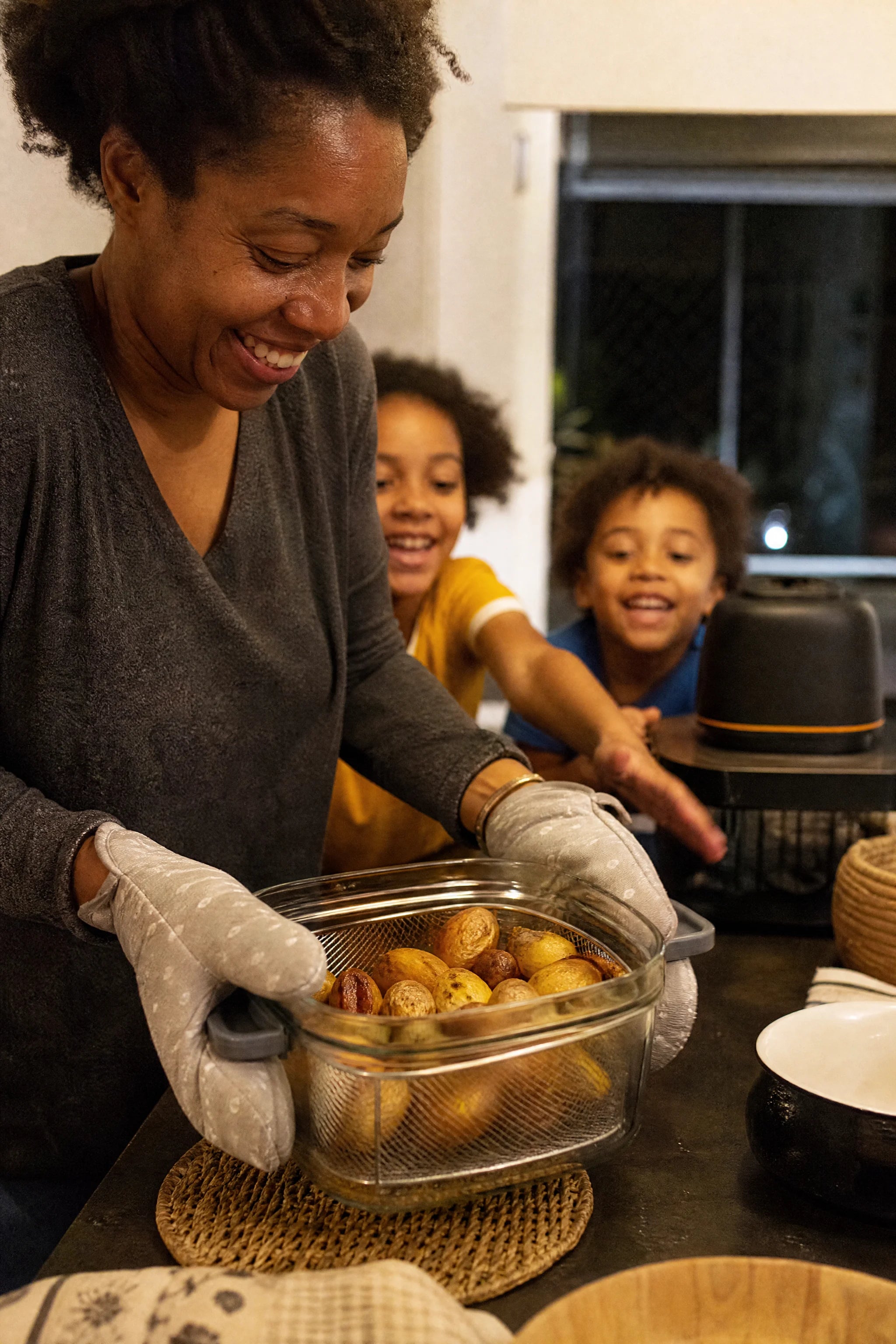 A mother lifting the glass bowl of Kaldera Glass full of roasted potatoes onto the family table